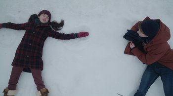 Movie still from “Snow Day” (2022), directed by Michael Lembeck – Two young girls laying in the middle of the snow making a snow angel; Wide shot, Overhead angle