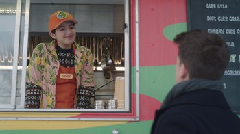 Movie still from “Snow Day” (2022), directed by Michael Lembeck – A woman in an orange hat is behind the counter of a food truck; Medium shot, Over the shoulder angle