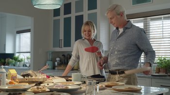 Movie still from “Snow Day” (2022), directed by Michael Lembeck – A man and a woman standing in front of a table with food on it; Medium shot, Over the shoulder angle