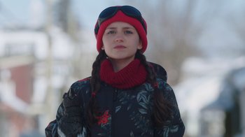 Movie still from “Snow Day” (2022), directed by Michael Lembeck – A young woman wearing a red hat and a red scarf; Medium shot, Low angle
