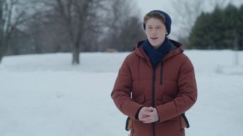 Movie still from “Snow Day” (2022), directed by Michael Lembeck – A young man in a red jacket standing in the snow; Medium shot, Over the shoulder angle