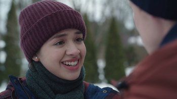 Movie still from “Snow Day” (2022), directed by Michael Lembeck – A young woman wearing a hat and a scarf smiling; Close Up shot, Over the shoulder angle