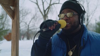 Movie still from “Snow Day” (2022), directed by Michael Lembeck – A man with a microphone in his mouth in the snow; Close Up shot, Low angle