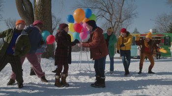 Movie still from “Snow Day” (2022), directed by Michael Lembeck – A group of people standing in the snow holding balloons; Wide shot, High angle