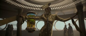 Movie still from “Solo: A Star Wars Story” (2018), directed by Ron Howard – A woman in a gold dress holding a jar; Medium shot, Low angle