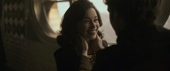 Movie still from “Solo: A Star Wars Story” (2018), directed by Ron Howard – A young woman smiles at the camera while holding her hands to her face; Close Up shot, Over the shoulder angle