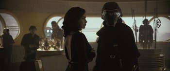 Movie still from “Solo: A Star Wars Story” (2018), directed by Ron Howard – A woman standing next to a man in a suit; Medium shot, Over the shoulder angle