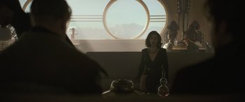 Movie still from “Solo: A Star Wars Story” (2018), directed by Ron Howard – A woman sitting on a couch in front of a round window; Wide shot, Over the shoulder angle
