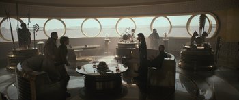 Movie still from “Solo: A Star Wars Story” (2018), directed by Ron Howard – A group of people sitting at a table in front of a large window; Wide shot, High angle