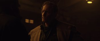 Movie still from “Solo: A Star Wars Story” (2018), directed by Ron Howard – A man with a beard is standing in the dark; Close Up shot, Over the shoulder angle