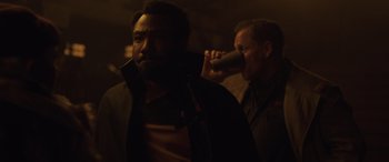 Movie still from “Solo: A Star Wars Story” (2018), directed by Ron Howard – A man drinking from a cup while another man looks on; Medium shot, Over the shoulder angle