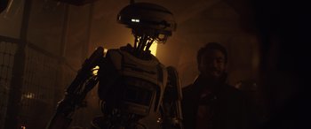 Movie still from “Solo: A Star Wars Story” (2018), directed by Ron Howard – A man standing next to a robot in the dark; Medium shot, Low angle