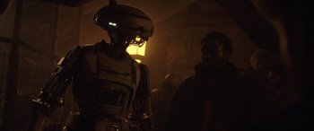 Movie still from “Solo: A Star Wars Story” (2018), directed by Ron Howard – A man standing next to a robot in a dark room; Medium shot, Over the shoulder angle