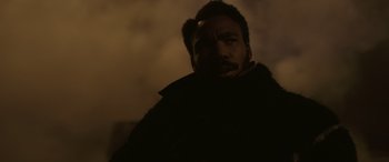 Movie still from “Solo: A Star Wars Story” (2018), directed by Ron Howard – A man with a beard is standing in the dark; Close Up shot, Over the shoulder angle