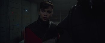 Movie still from “Solo: A Star Wars Story” (2018), directed by Ron Howard – A woman in a black , red and white jacket; Close Up shot, Over the shoulder angle