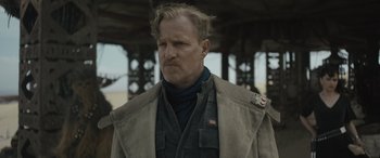 Movie still from “Solo: A Star Wars Story” (2018), directed by Ron Howard – A man in a trench coat standing in front of a metal structure; Close Up shot, Over the shoulder angle