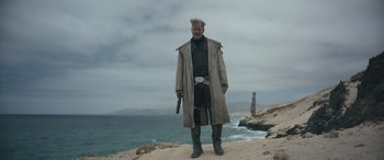 Movie still from “Solo: A Star Wars Story” (2018), directed by Ron Howard – An old man standing on the beach holding a gun; Medium shot, Low angle