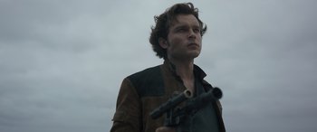 Movie still from “Solo: A Star Wars Story” (2018), directed by Ron Howard – A man holding a gun while standing in a field; Close Up shot, Low angle