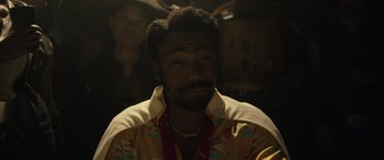 Movie still from “Solo: A Star Wars Story” (2018), directed by Ron Howard – A man in a yellow shirt is looking at the camera; Close Up shot, Over the shoulder angle