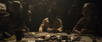 Movie still from “Solo: A Star Wars Story” (2018), directed by Ron Howard – A person sitting at a table with a lot of broken cds; Medium shot, Over the shoulder angle