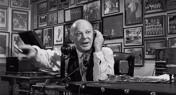 Movie still from “Some Like It Hot” (1959), directed by Billy Wilder – An older man sitting at a desk talking on a phone; Medium shot, Low angle