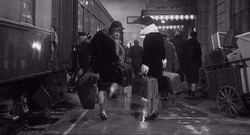 Movie still from “Some Like It Hot” (1959), directed by Billy Wilder – Two women are carrying suitcases in the rain; Wide shot, Low angle