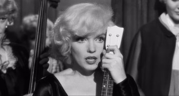 Movie still from “Some Like It Hot” (1959), directed by Billy Wilder – A woman holding up a guitar in front of her face; Close Up shot, Over the shoulder angle
