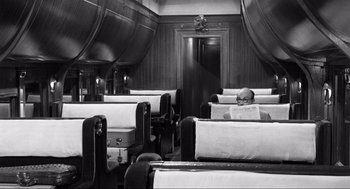 Movie still from “Some Like It Hot” (1959), directed by Billy Wilder – A man sitting on a train reading a newspaper; Wide shot, High angle