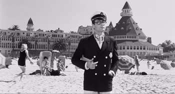 Movie still from “Some Like It Hot” (1959), directed by Billy Wilder – A man in a sailor's uniform standing on the beach in front of a building; Wide shot, Low angle