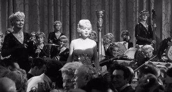 Movie still from “Some Like It Hot” (1959), directed by Billy Wilder – A woman standing in front of a crowd of people; Wide shot, Low angle