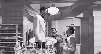 Movie still from “Some Like It Hot” (1959), directed by Billy Wilder – A man in a white suit is standing next to a man in a black suit; Wide shot, Over the shoulder angle