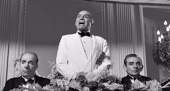 Movie still from “Some Like It Hot” (1959), directed by Billy Wilder – An old photo of a man in a suit and bow tie singing; Medium shot, Low angle