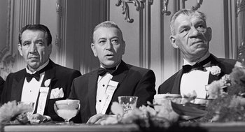 Movie still from “Some Like It Hot” (1959), directed by Billy Wilder – A black - and - white photo of three men sitting at a table; Medium shot, Low angle