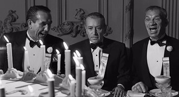 Movie still from “Some Like It Hot” (1959), directed by Billy Wilder – A man sitting at a dinner table in front of candles; Medium shot, Over the shoulder angle