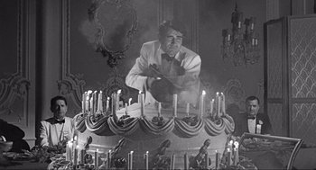 Movie still from “Some Like It Hot” (1959), directed by Billy Wilder – A man in a white suit is lighting candles on a cake; Medium shot, Overhead angle