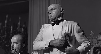 Movie still from “Some Like It Hot” (1959), directed by Billy Wilder – A man in a white suit and bow tie holding a microphone; Medium shot, Low angle