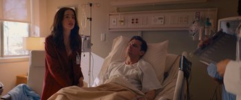 Movie still from “Something from Tiffany's” (2022), directed by Daryl Wein – A woman standing next to a man laying in a hospital bed; Medium shot, Over the shoulder angle