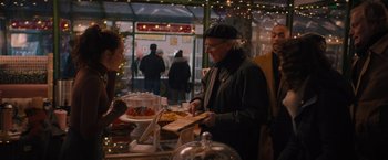 Movie still from “Something from Tiffany's” (2022), directed by Daryl Wein – An older man is serving food to a crowd; Medium shot, Over the shoulder angle