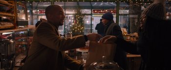 Movie still from “Something from Tiffany's” (2022), directed by Daryl Wein – A man is handing something to another man in front of a christmas tree; Medium shot, Over the shoulder angle