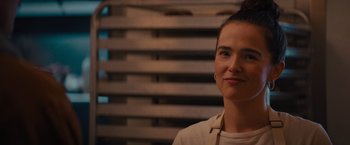 Movie still from “Something from Tiffany's” (2022), directed by Daryl Wein – A woman is smiling for the camera in front of a wooden wall; Close Up shot, Over the shoulder angle