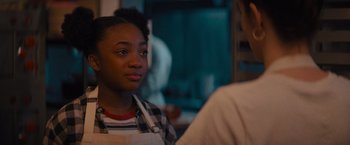 Movie still from “Something from Tiffany's” (2022), directed by Daryl Wein – A young woman wearing an apron in a kitchen; Close Up shot, Over the shoulder angle