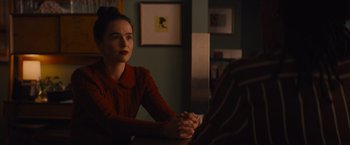 Movie still from “Something from Tiffany's” (2022), directed by Daryl Wein – A woman sitting at a table in a dark room; Medium shot, Over the shoulder angle