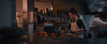 Movie still from “Something from Tiffany's” (2022), directed by Daryl Wein – A woman preparing food in a restaurant kitchen; Medium shot, Low angle