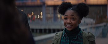 Movie still from “Something from Tiffany's” (2022), directed by Daryl Wein – A young girl smiles brightly while standing on a pier; Close Up shot, Over the shoulder angle