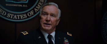 Movie still from “Sonic the Hedgehog” (2020), directed by Jeff Fowler – An older man in a military uniform is in front of a flag; Close Up shot, Over the shoulder angle