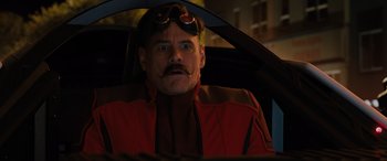 Movie still from “Sonic the Hedgehog” (2020), directed by Jeff Fowler – A man in a red jacket with a mustache and a goatee sitting in the driver's seat of a car; Close Up shot, Over the shoulder angle