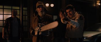 Movie still from “Sonic the Hedgehog” (2020), directed by Jeff Fowler – A man holding a chain saw while another man takes a picture; Medium shot, Over the shoulder angle