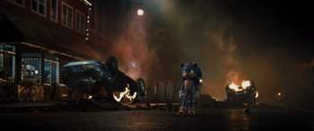 Movie still from “Sonic the Hedgehog” (2020), directed by Jeff Fowler – A sonic the hedgehog character standing in front of a burning car; Wide shot, Over the shoulder angle