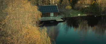 Movie still from “Soulcatcher” (2023), directed by Daniel Markowicz – A house with solar panels on the roof by the water; Extreme Wide shot, High angle