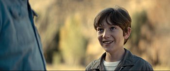 Movie still from “Brightburn” (2019), directed by David Yarovesky – A young boy smiling for the camera with trees in the background; Close Up shot, Over the shoulder angle